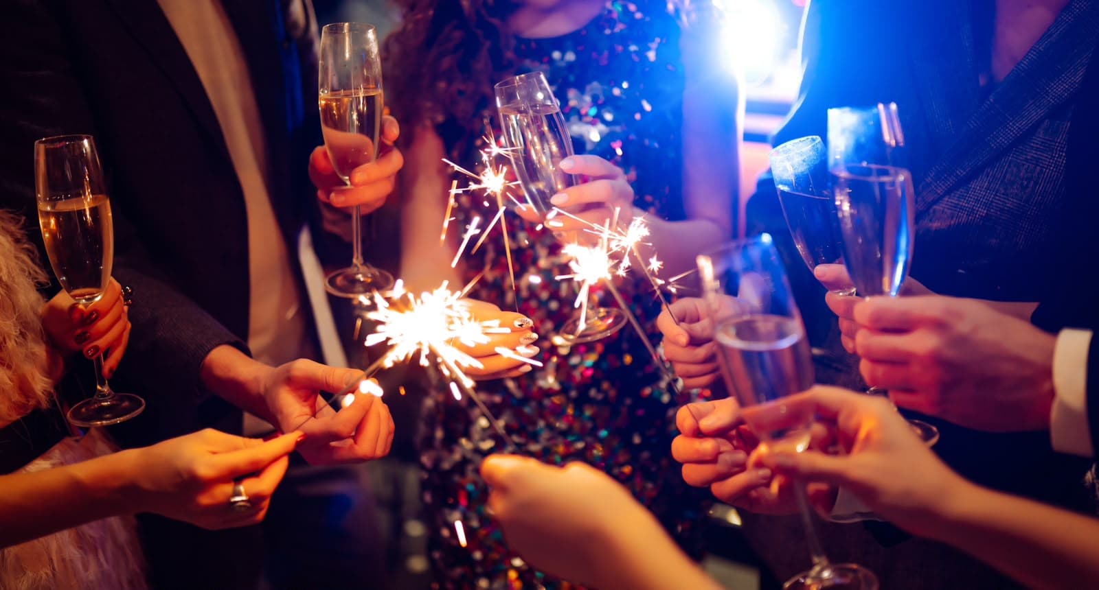 Feiernde Gäste stoßen am Abend mit Sektgläsern an und halten Wunderkerzen