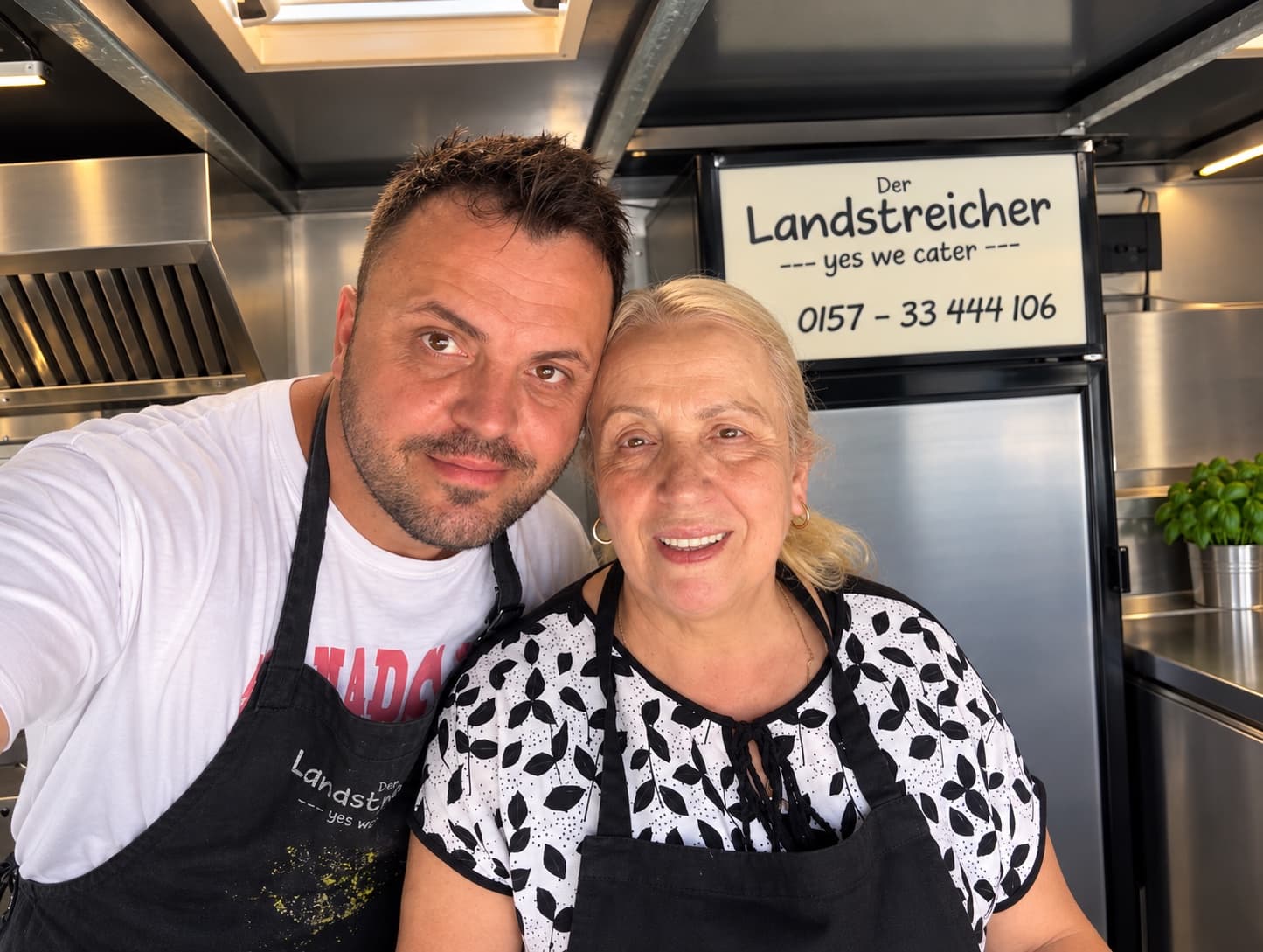 Das Landstreicher-Team: zwei Menschen in schwarzen Landstreicher-Schürzen lächeln gemeinsam in der Truck-Küche
